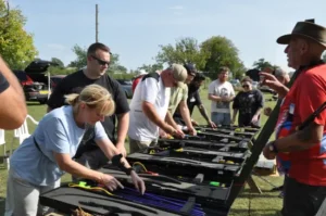 A man in a red coaching shirt instructing a group of people on how to assemble a modern archery bow
