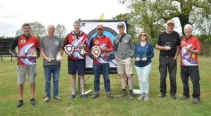 A group of people holding awards in front of an archery target