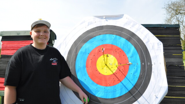 Junior archer from the April 2026 beginners class standing in front of a target with three arrows in the gold.