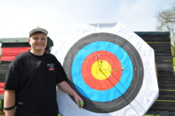 Junior archer from the April 2026 beginners class standing in front of a target with three arrows in the gold.