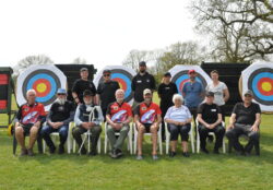 A group of people lined up for a group photo in front of archery targets.
