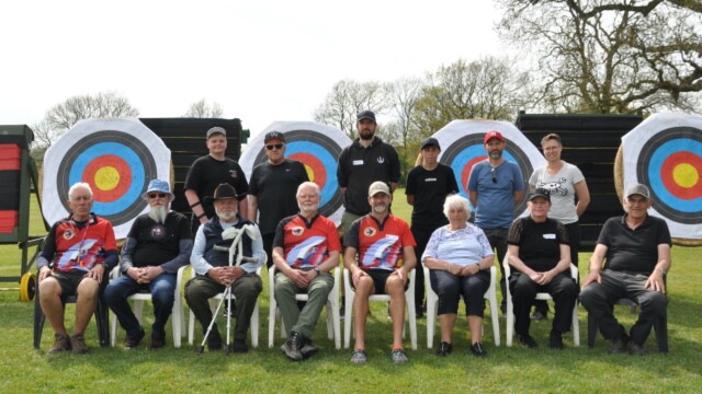 A group of people lined up for a group photo in front of archery targets.